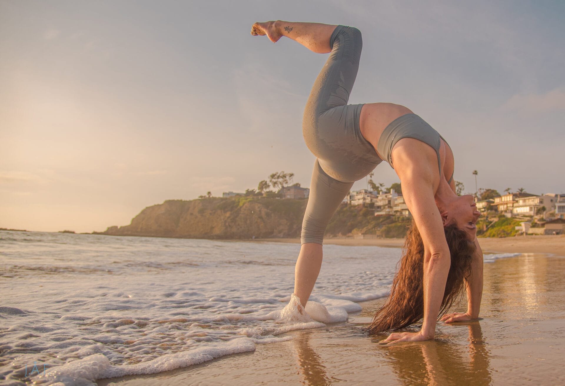 Woman performing a backbend on a beach at sunset.