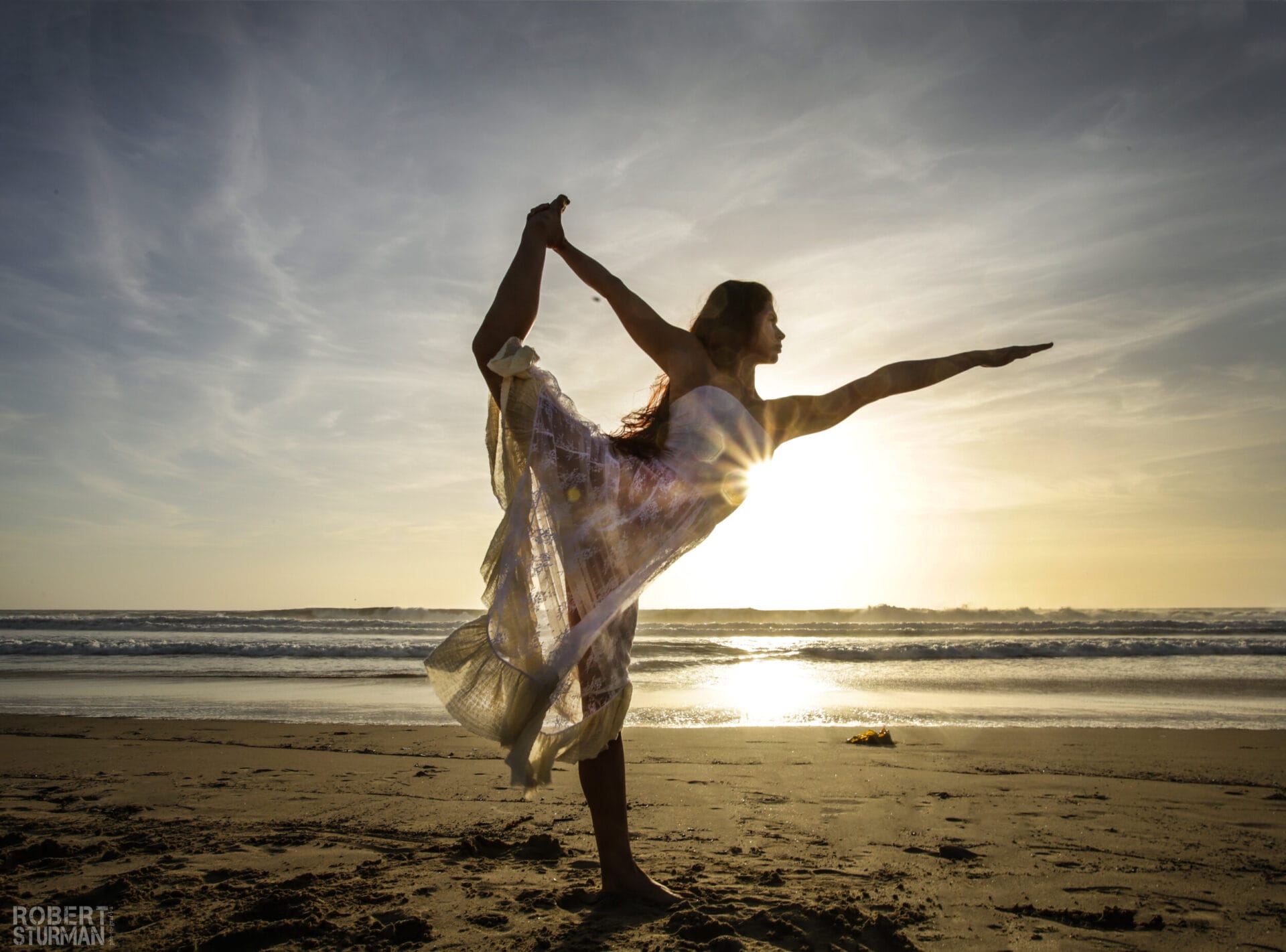 A person performing a yoga pose on the beach at sunset.