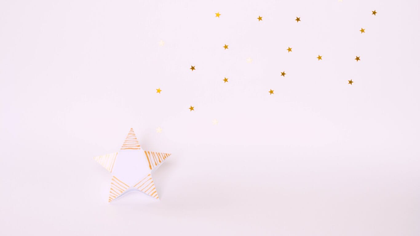 A paper star with stripes and small golden star stickers scattered on a white background.