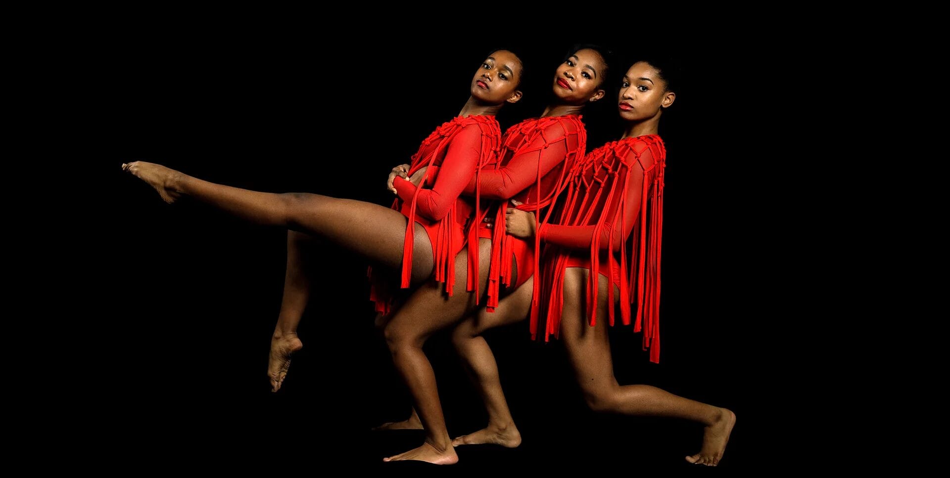 Three dancers in red fringe costumes posing against a black background.